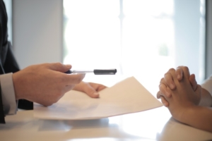 Person holding out pen and paper to someone else